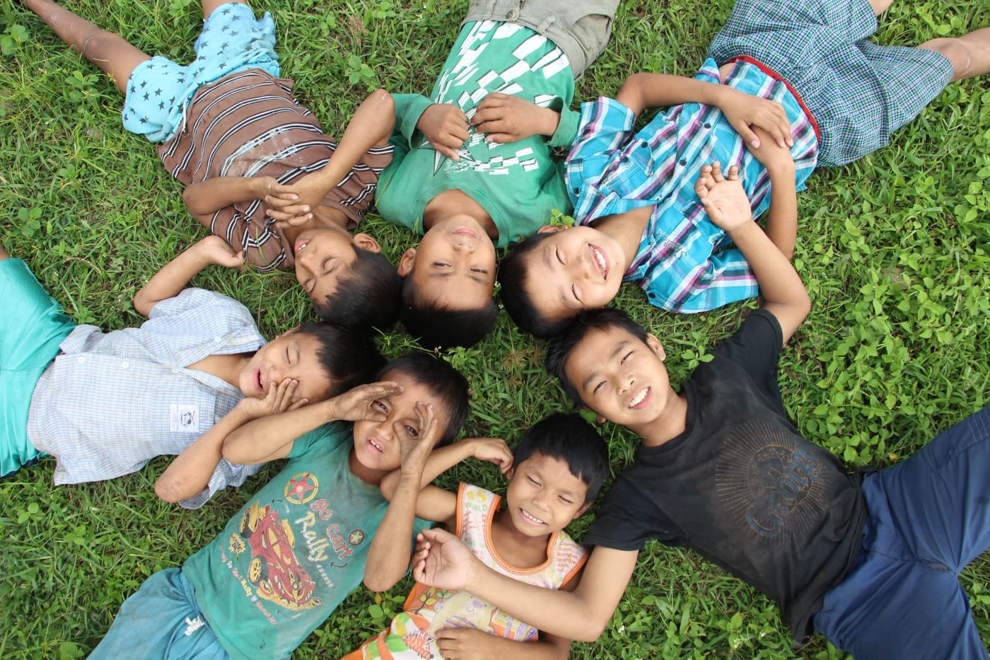 Seven boys lying in a circle on the grass, photographed from above