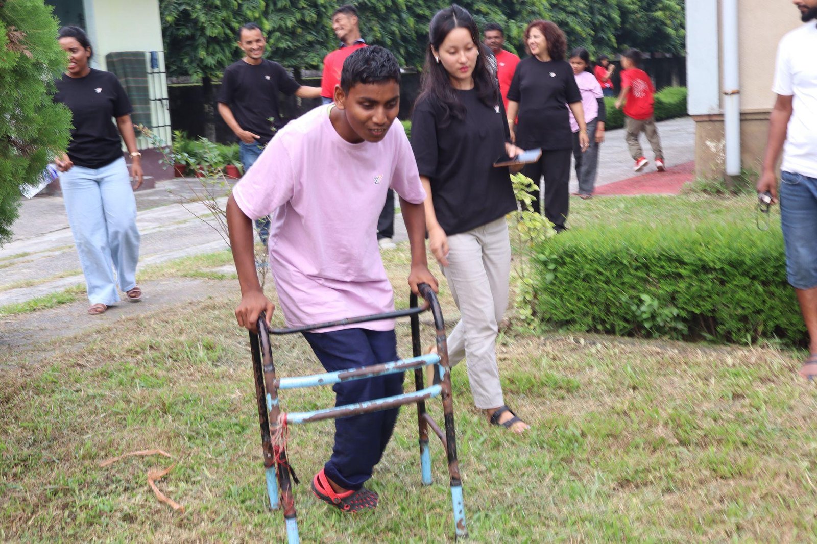 A boy using a mobility walker on a grassy lawn, accompanied by a young woman