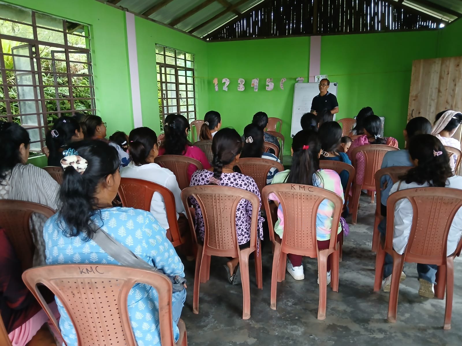 Community members seated at a health awareness session with a facilitator beside a whiteboard